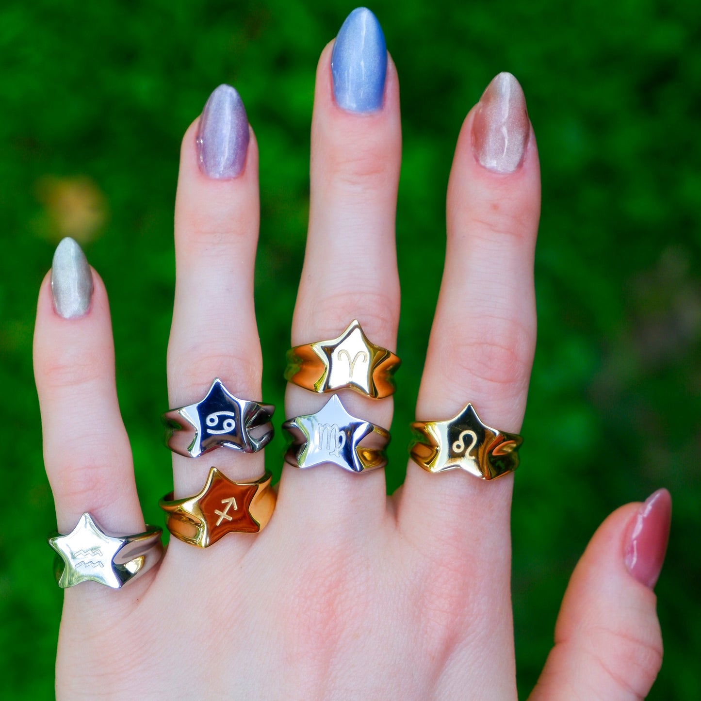 Hand wearing multiple star-shaped rings with a blurred green background