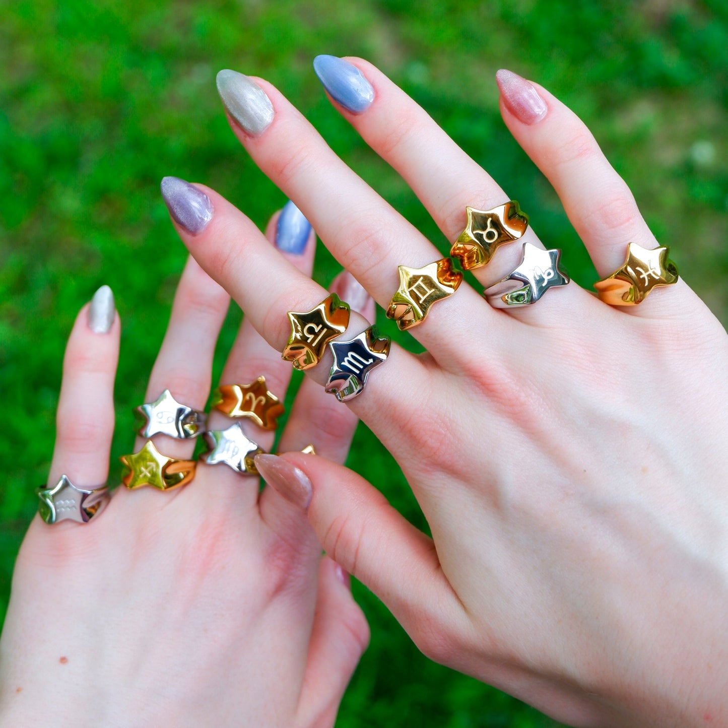 Two hands wearing multiple star-shaped rings against a blurred green background