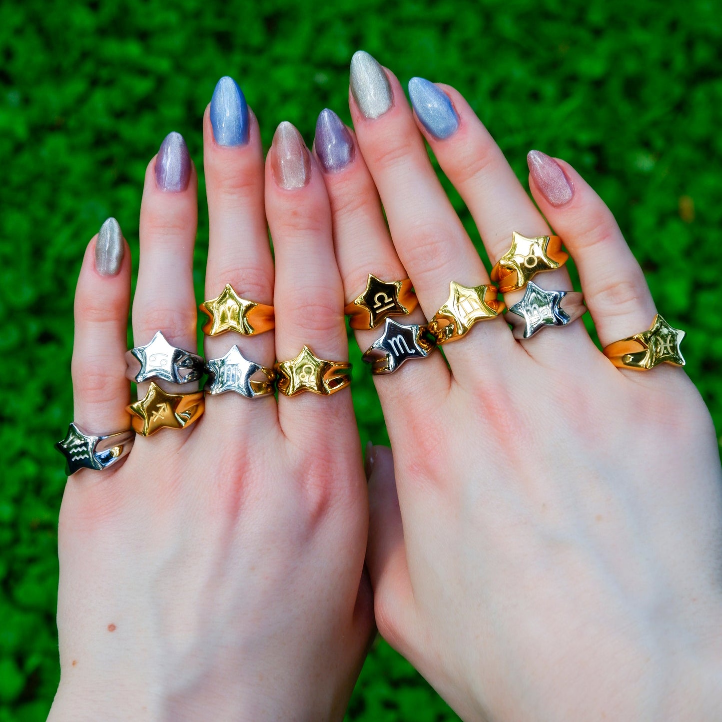 Two hands wearing multiple star-shaped rings on a green grass background