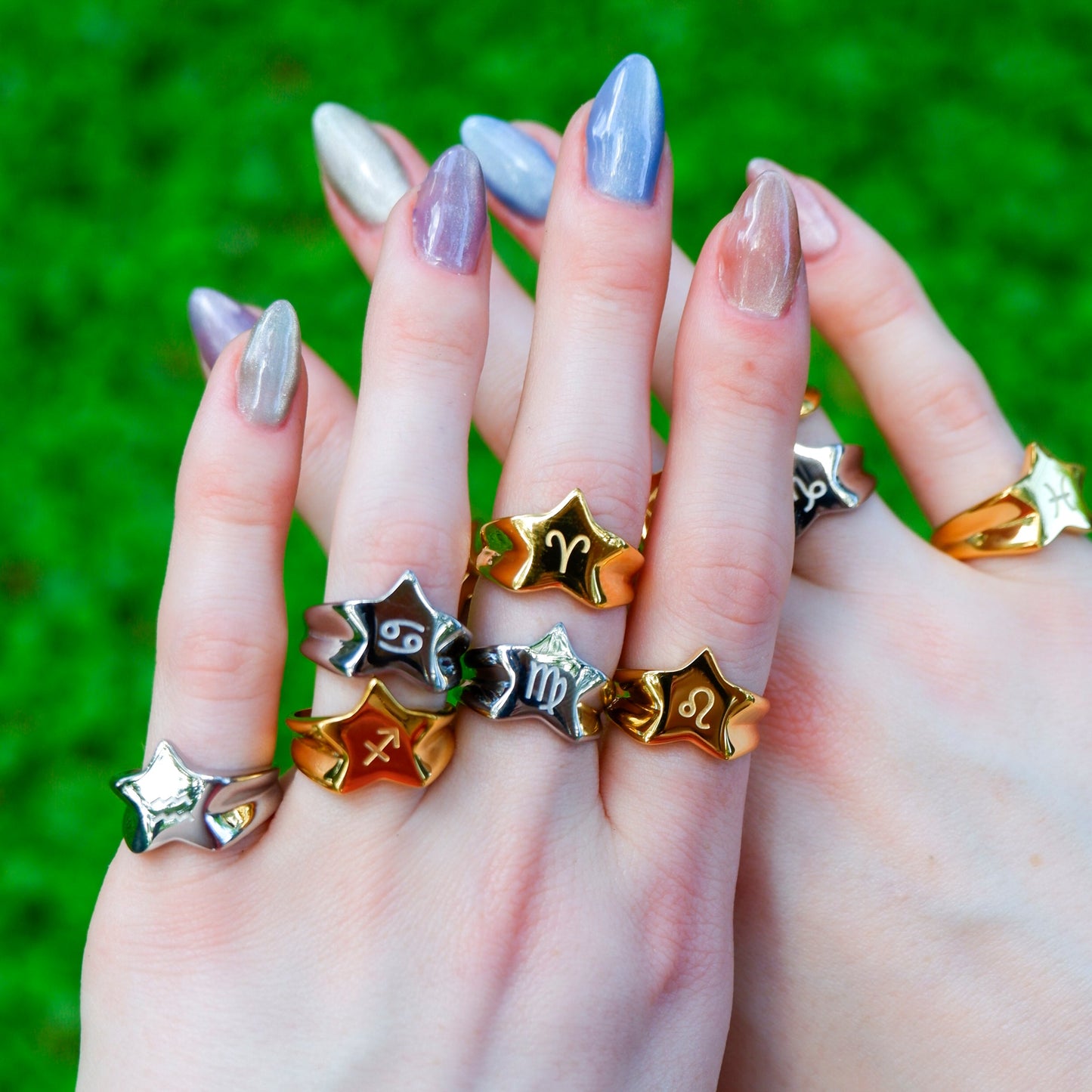Two hands wearing multiple star-shaped rings against a green grass background