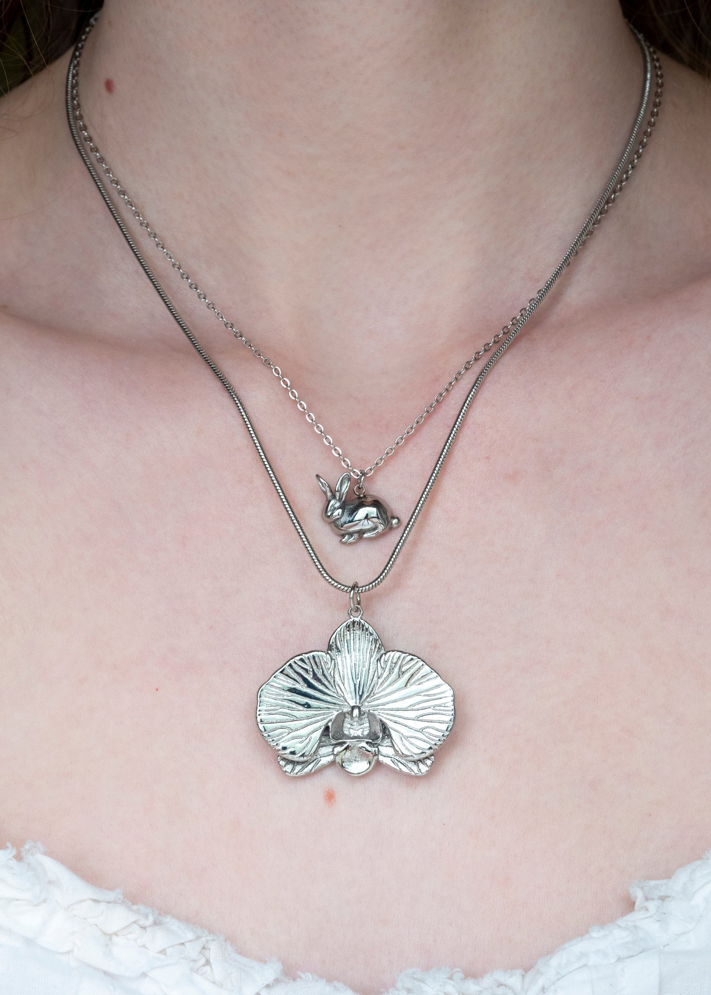 Silver necklace with a pendant on a person wearing a white lace garment.