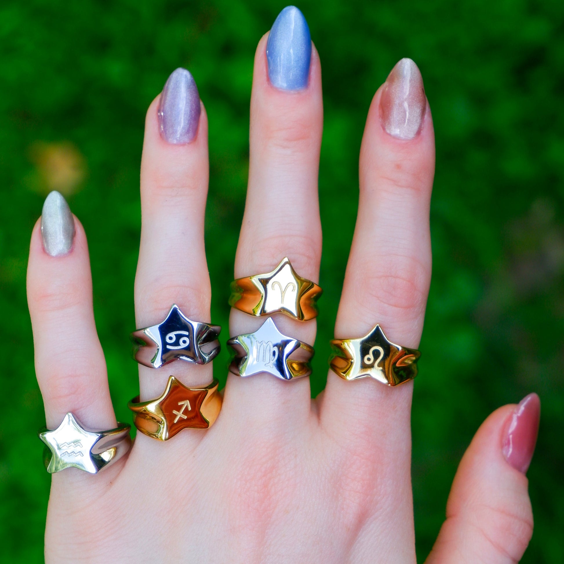 Hand wearing multiple star-shaped rings with a blurred green background