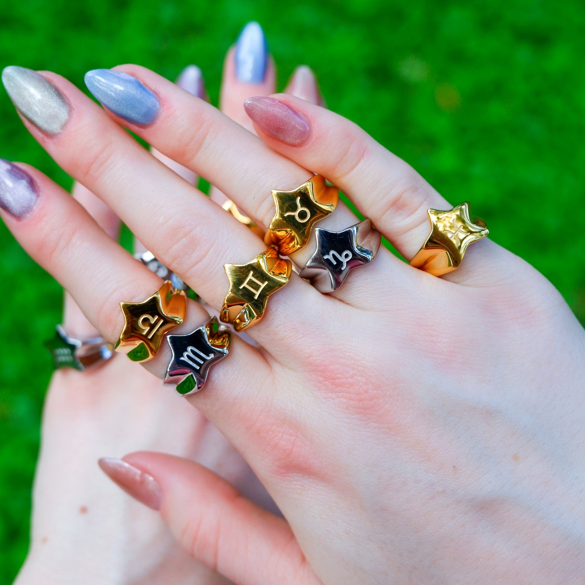 Hands wearing multiple star-shaped rings with different symbols against a green grass background