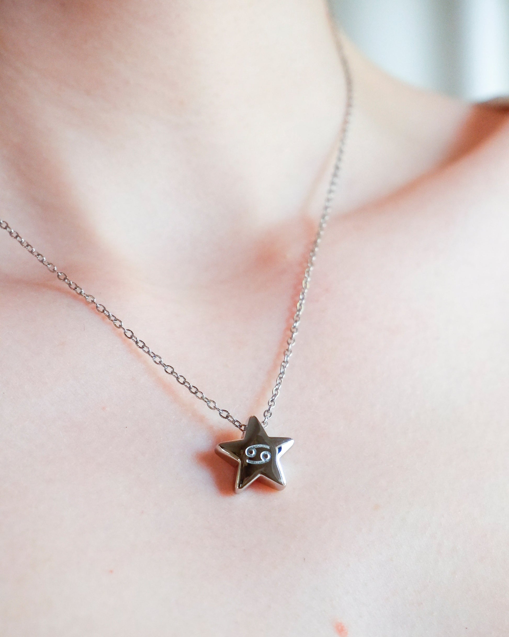 Silver star-shaped necklace with a small pendant on a person's neck against a neutral background