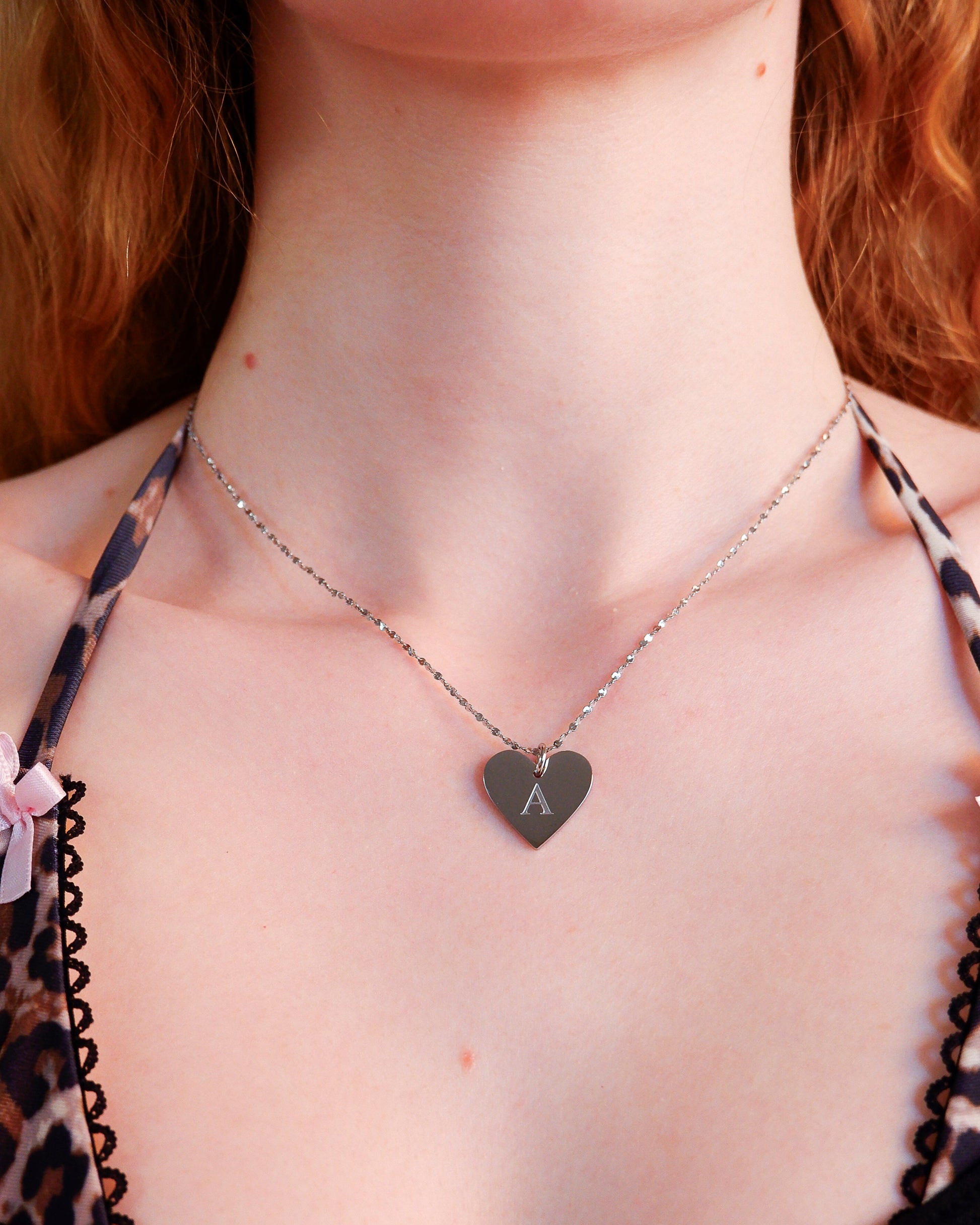 Heart-shaped necklace with a letter 'A' pendant worn by a person with red hair.
