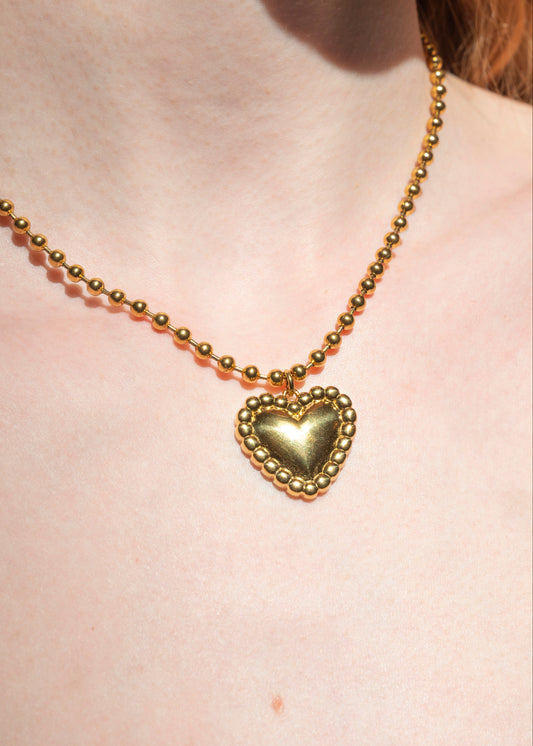 Gold beaded necklace with a heart pendant on a person's neck.