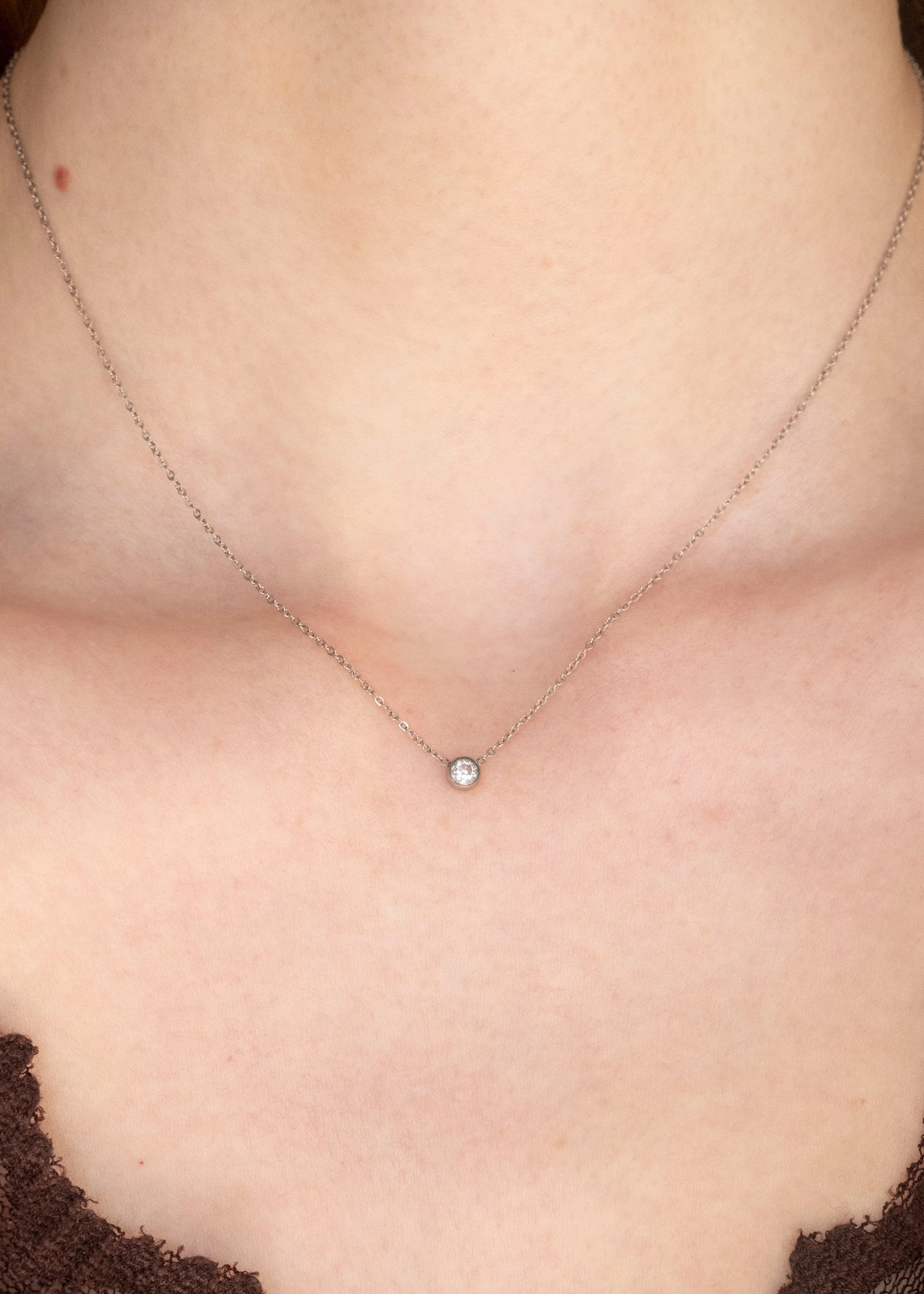 Close-up of a necklace with a small round pendant on a person's neck.