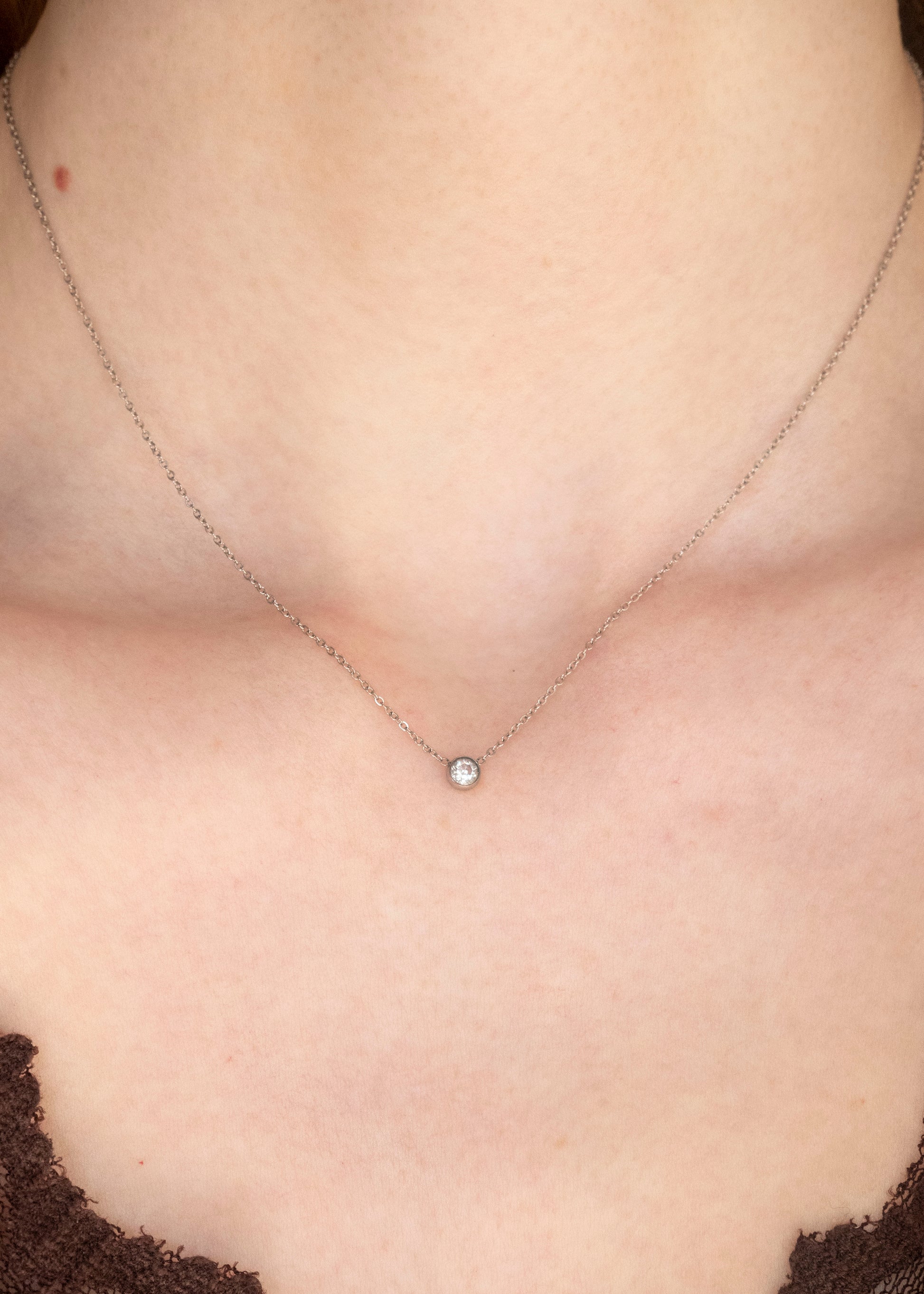 Close-up of a necklace with a small round pendant on a person's neck.