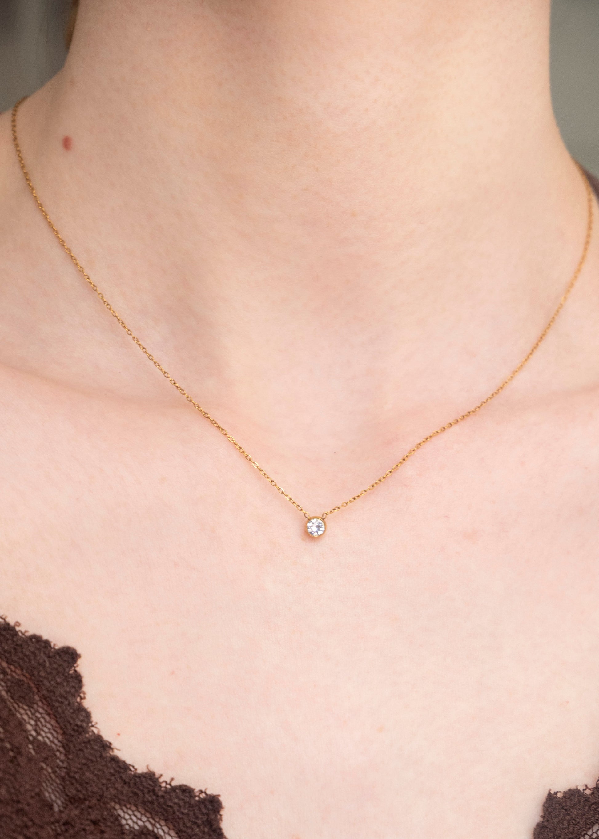 Gold necklace with a small pendant on a person wearing a brown lace garment.