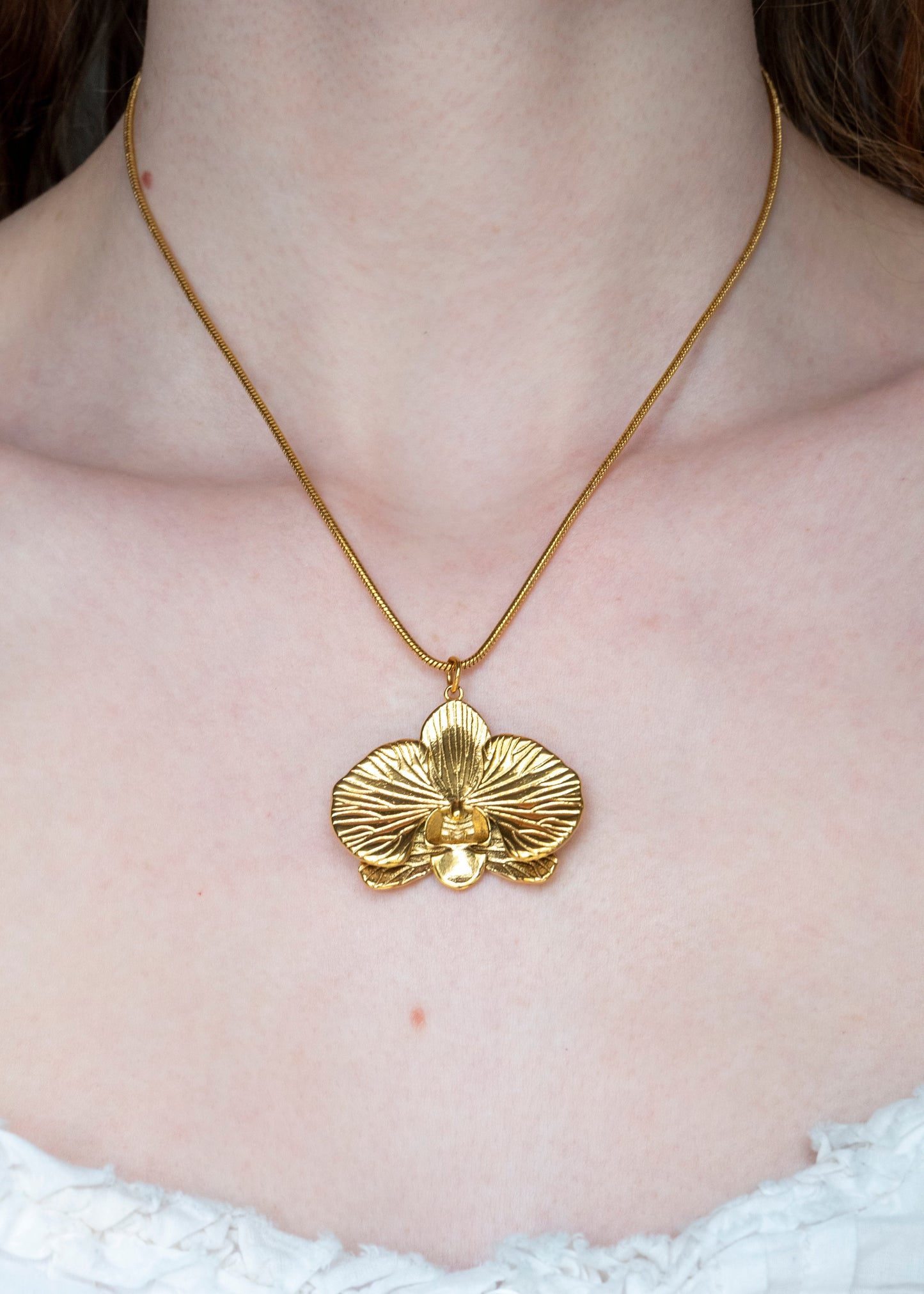 Gold orchid necklace on a person wearing a white top