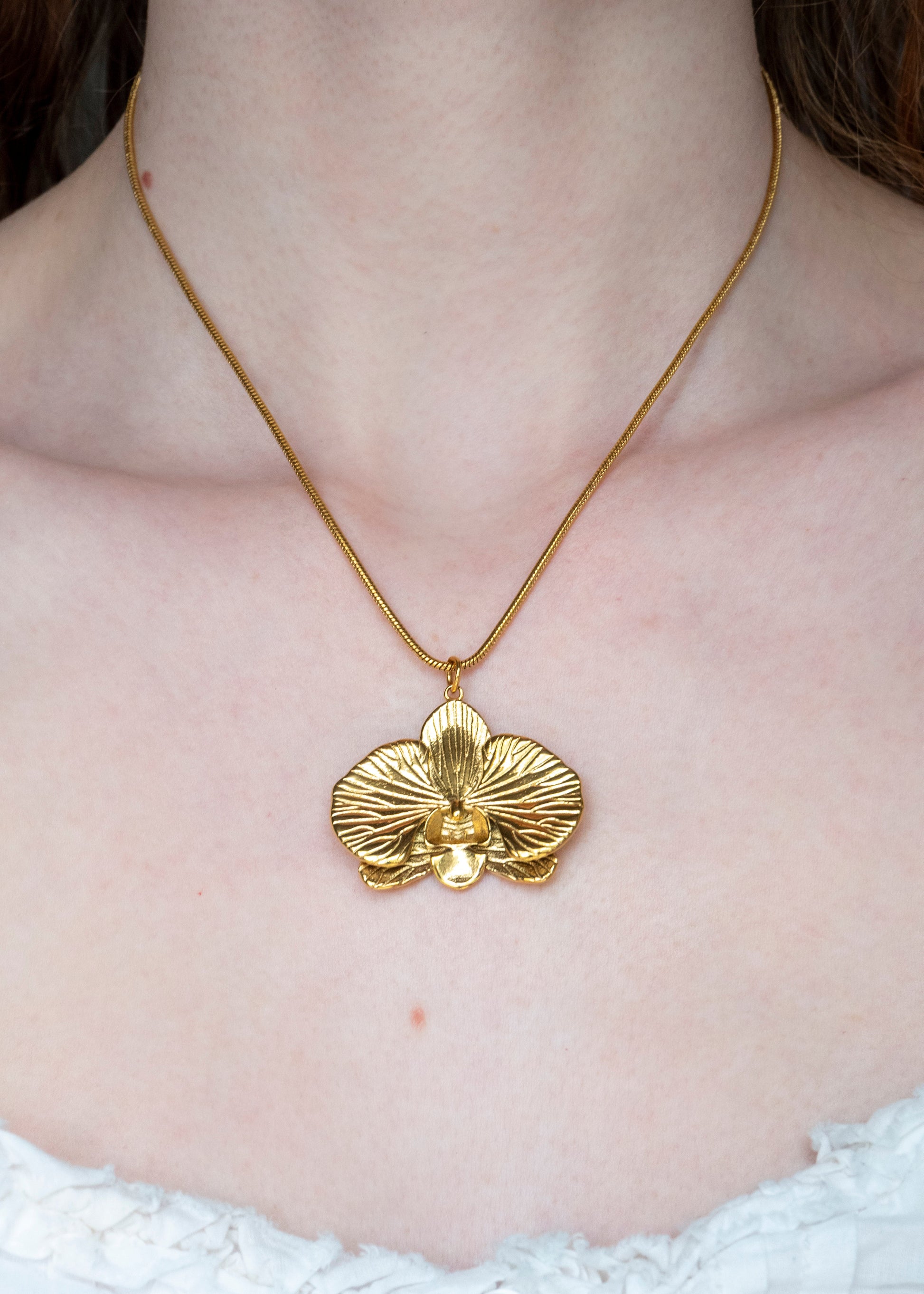 Gold orchid necklace on a person wearing a white top