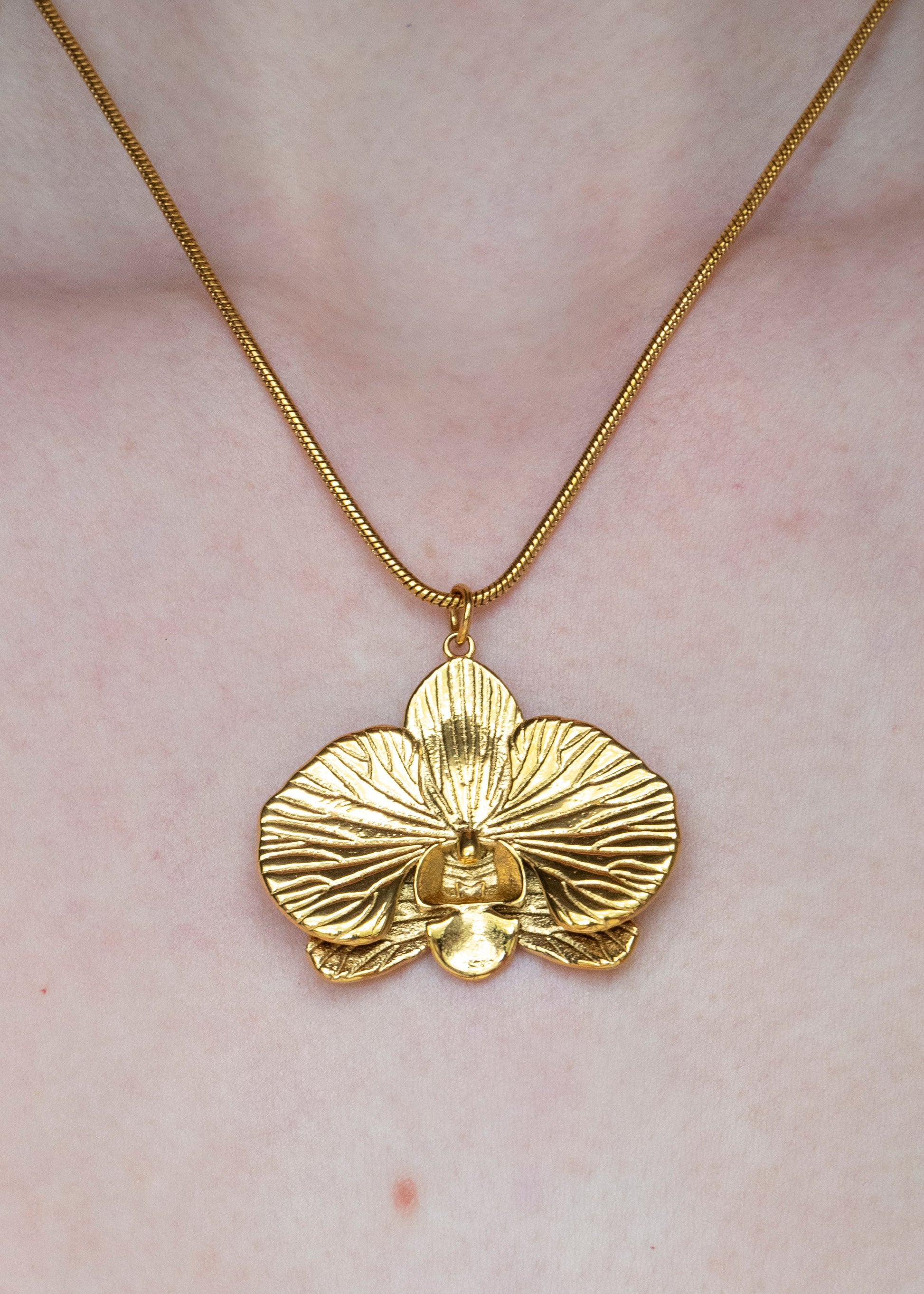 Gold orchid pendant necklace on a person wearing a white lace garment.