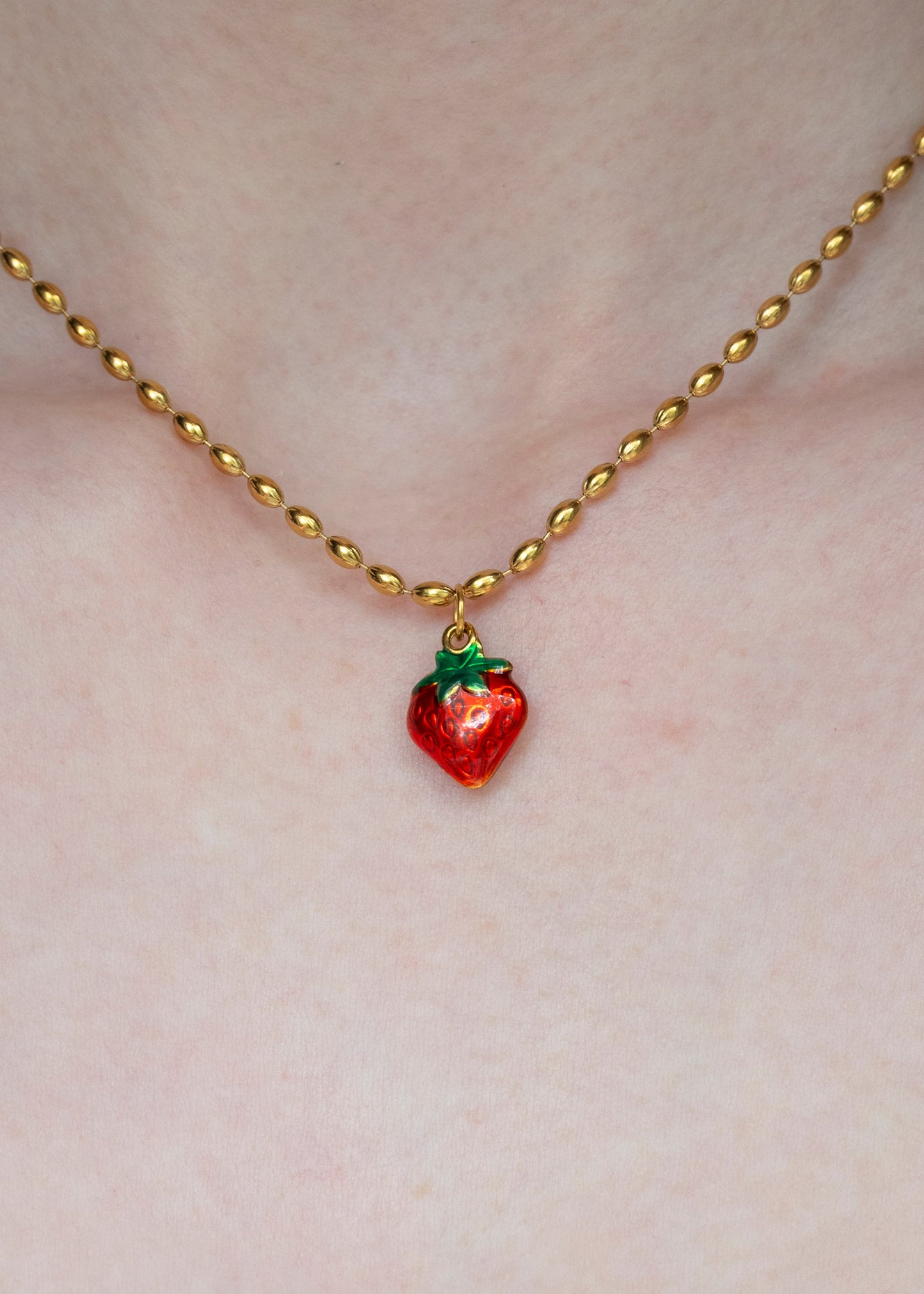 Gold necklace with a red strawberry pendant on a person's chest.