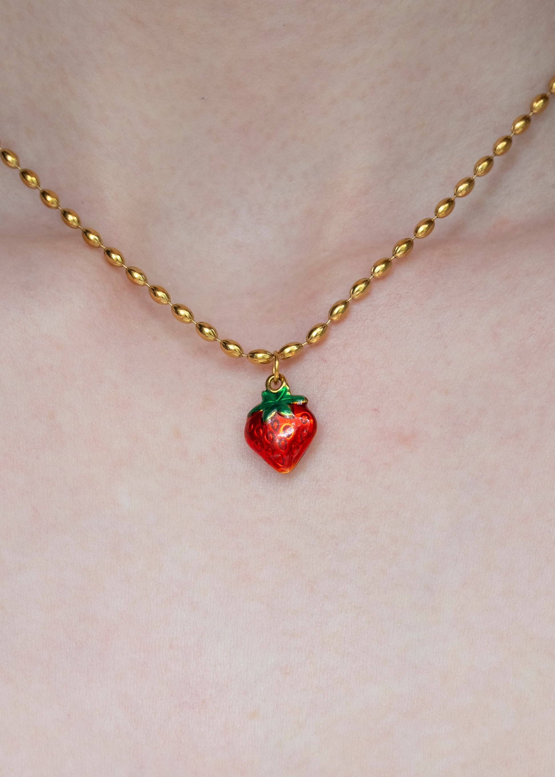 Gold necklace with a red strawberry pendant on a person's chest.