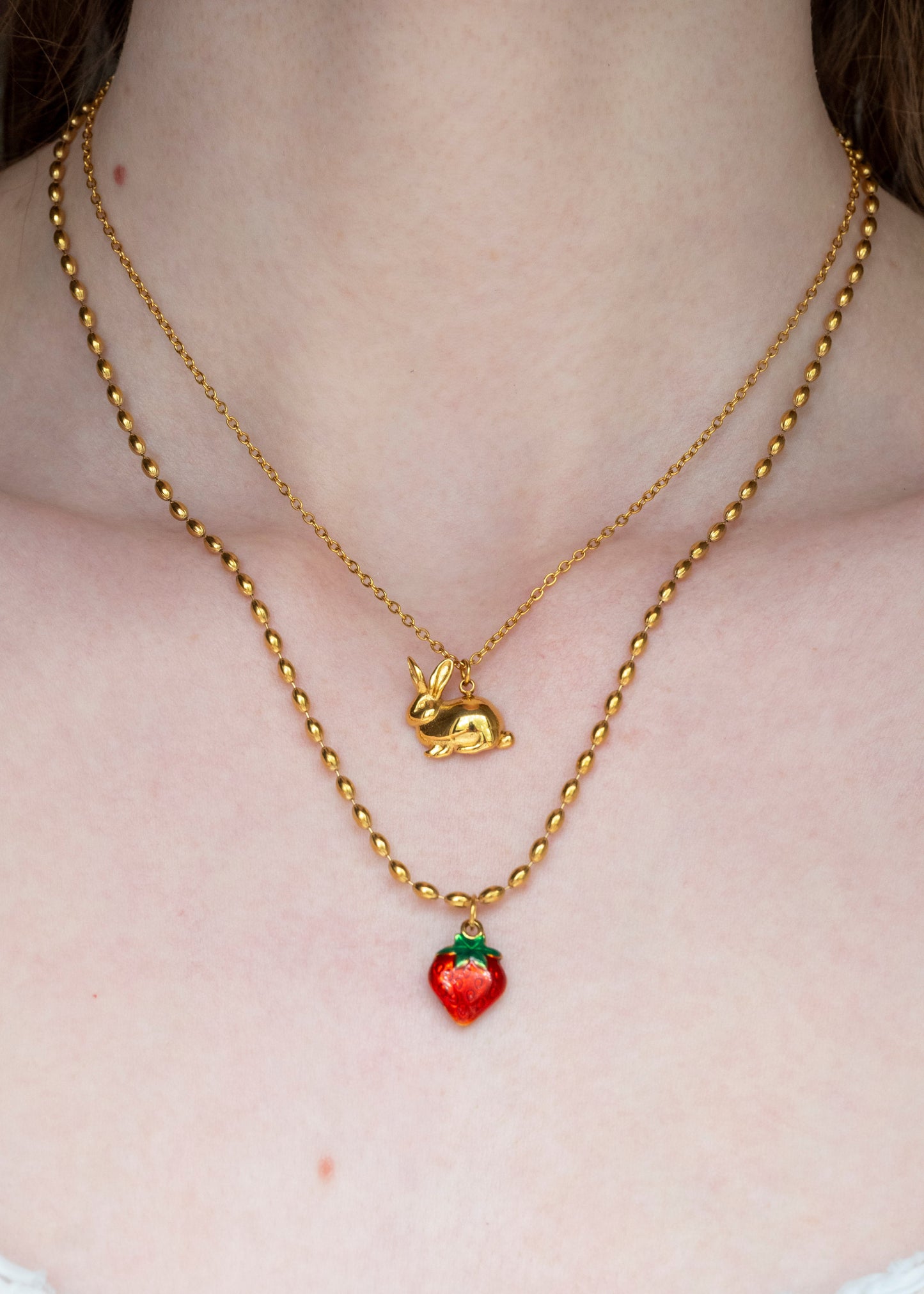 Gold necklace with a small red strawberry pendant on a plain background