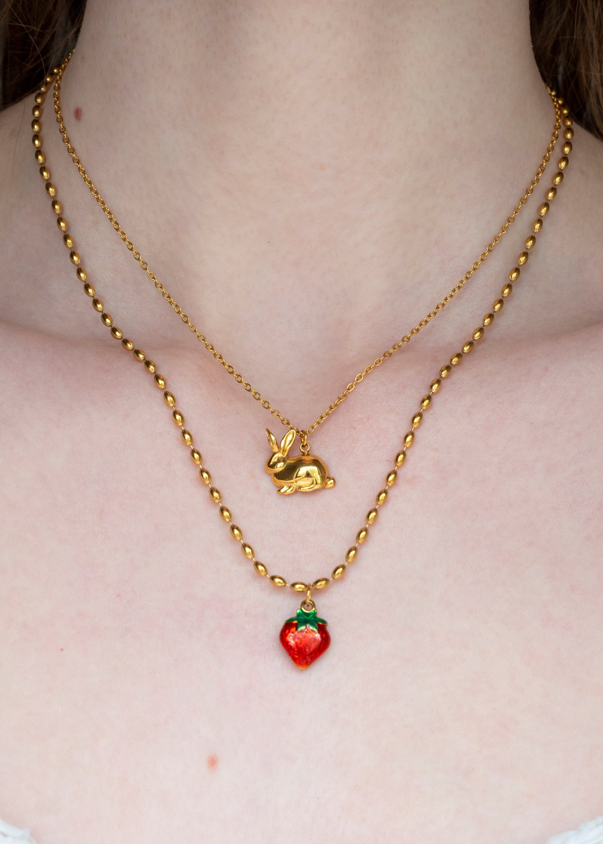 Gold necklace with a small red strawberry pendant on a plain background