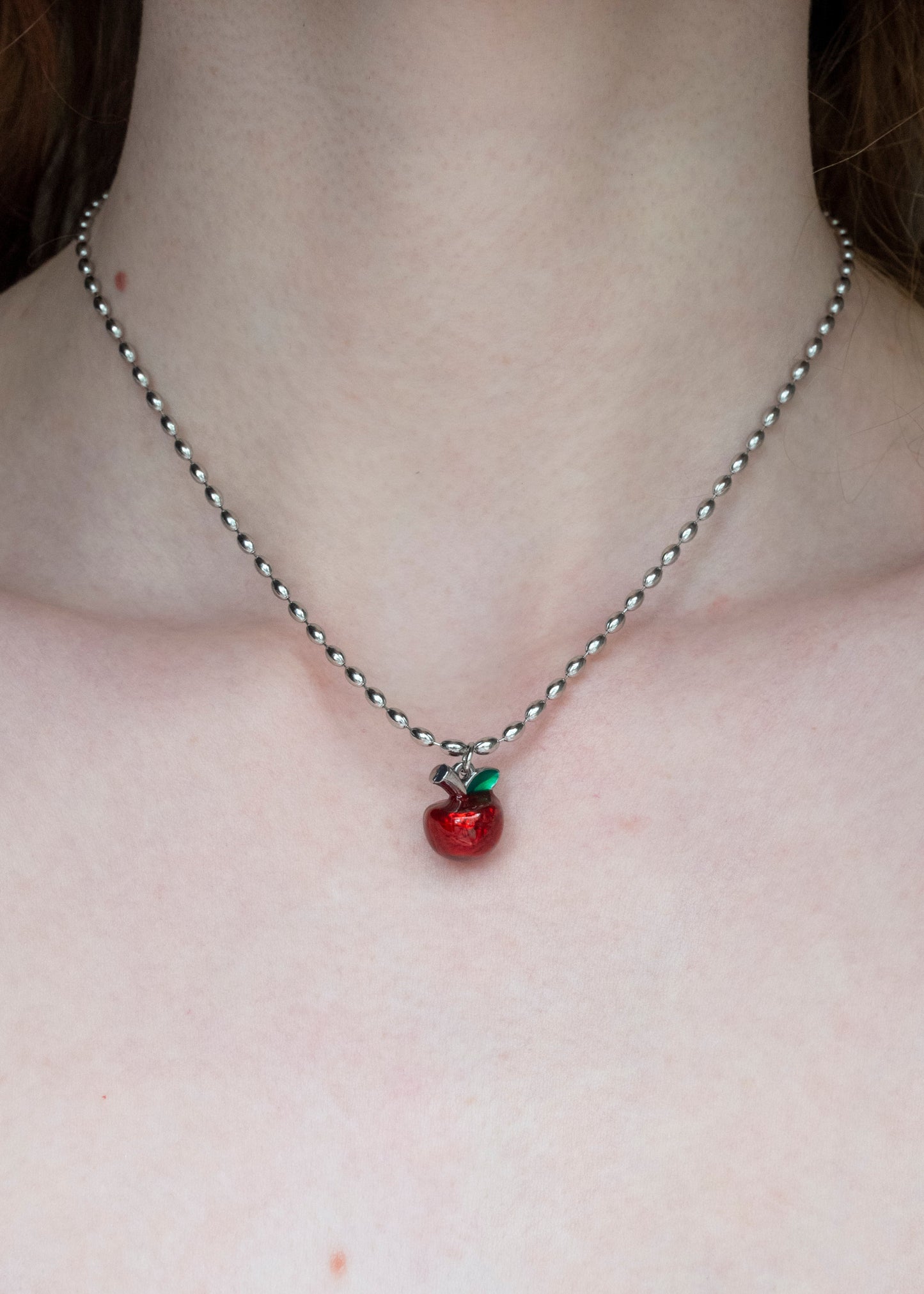 Necklace with a red apple pendant on a person's neck