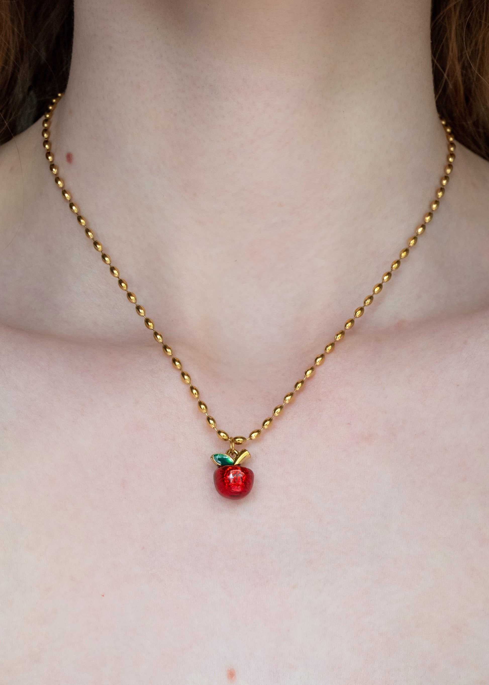 Gold necklace with a red apple pendant on a person's neck