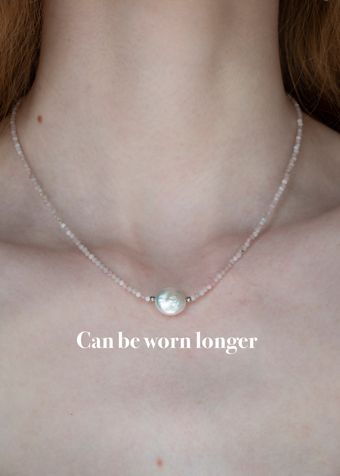 A close-up of a person's neck and upper chest wearing a delicate necklace with a single round pearl-like pendant on a thin pale chain. White text at the bottom reads 'Can be worn longer'.